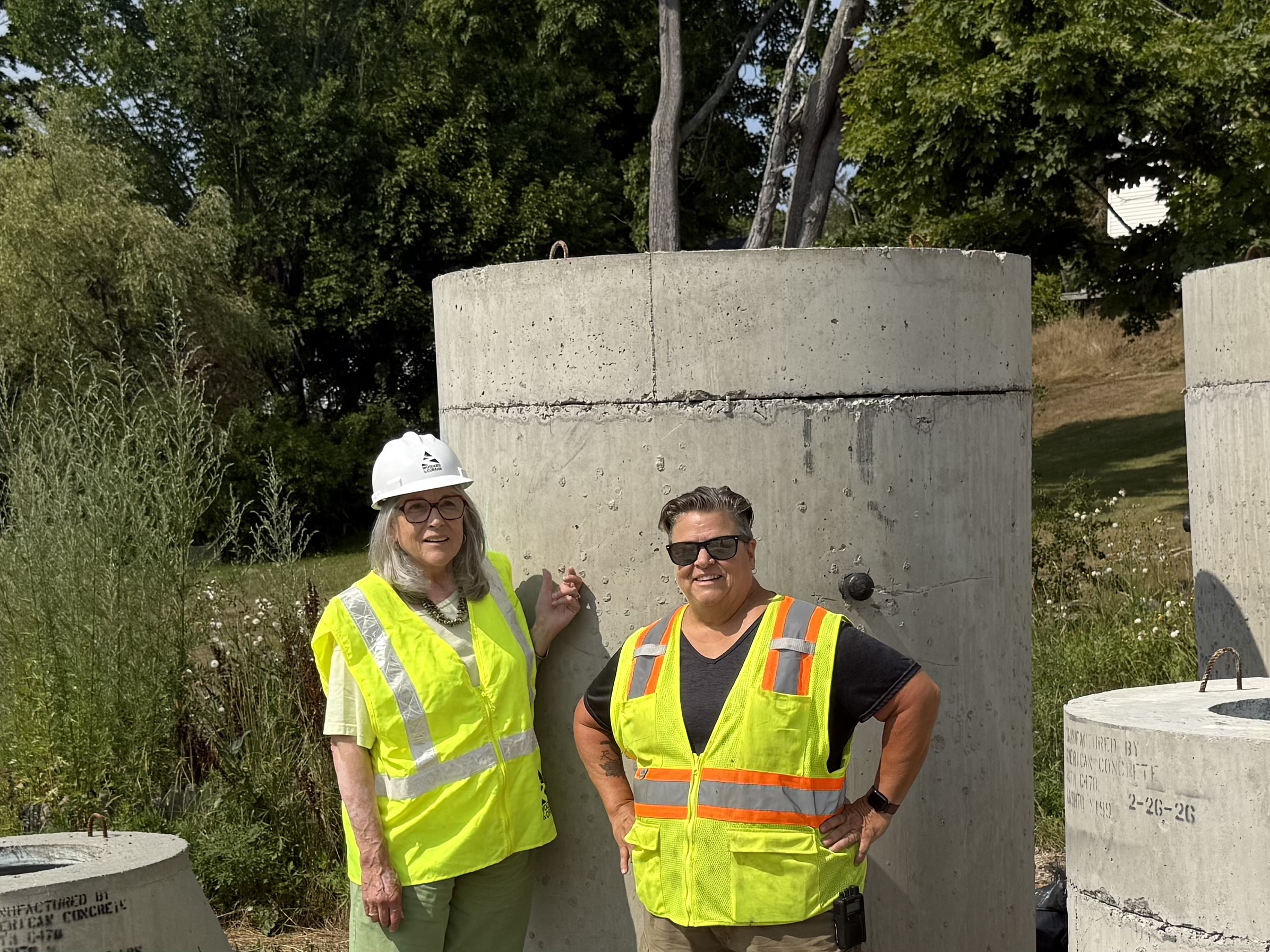 Two women in bright yellow construction vests standing next to a concrete structure.