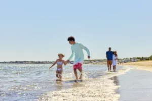 A family walking on the beach with a mother, father, son and daughter running through the water.